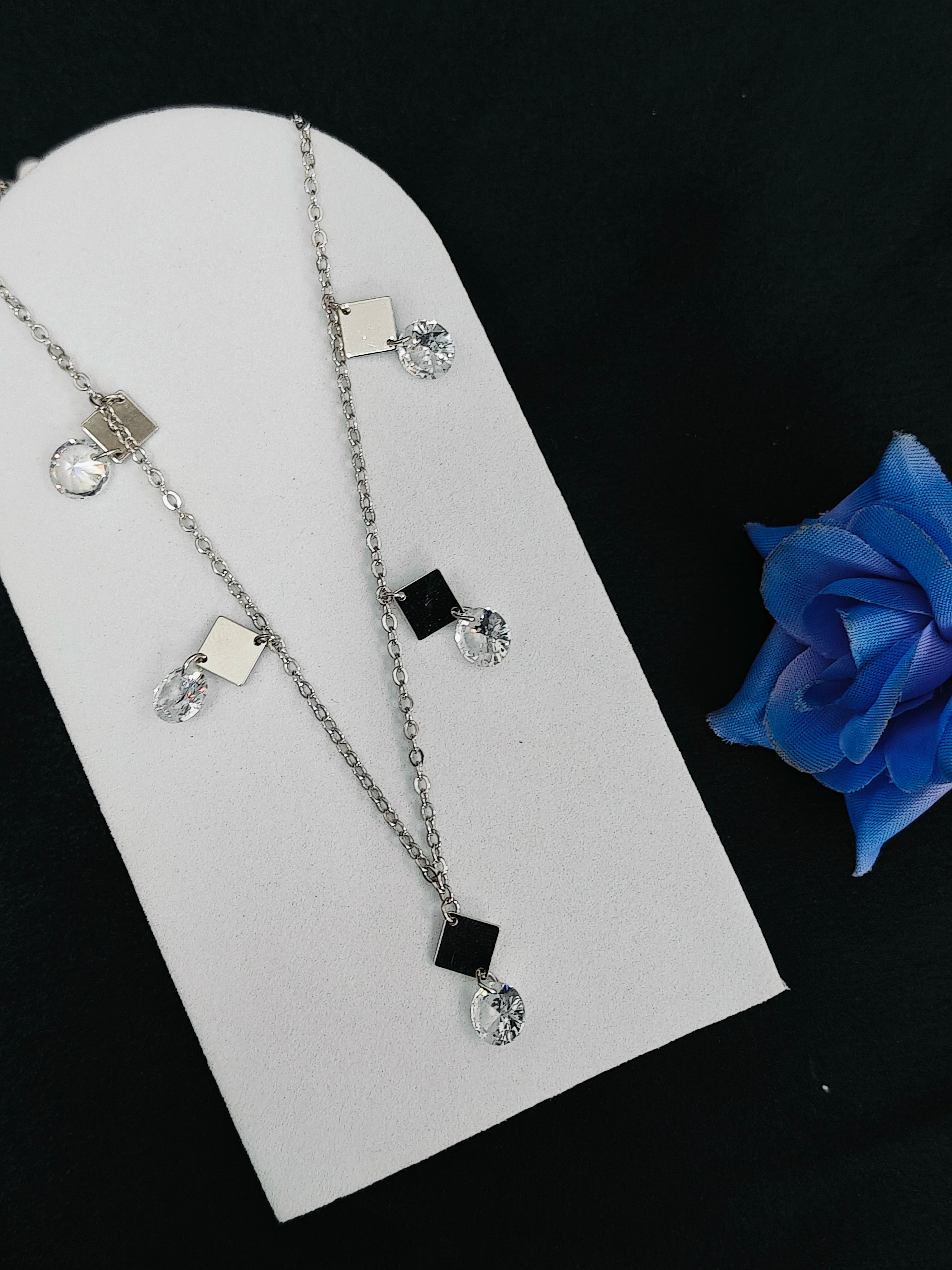 Necklace with pendant on a white stand with a blue rose in the background
